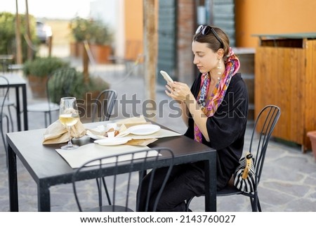 Woman takes photo on phone of food during a cheese tasting at local farm in Maremma region in Italy. Concept of Italian cuisine and local wine or cheese farms. Stylish woman with shawl in hair
