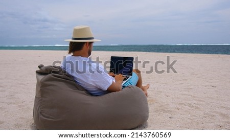 Freelance, travel and holidays concept. A man in yellow hat sitting on the beach background of the ocean. Work while on vacation at sea