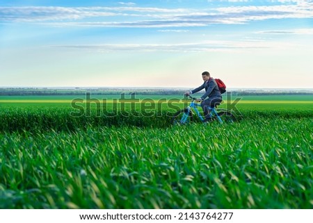a businessman rides a bicycle with a backpack through a green grass field, dressed in a business suit, beautiful nature in spring, business concept