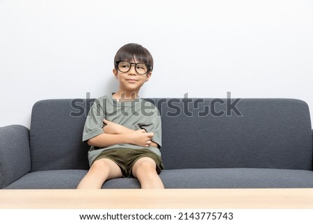 Cute asian boy with eyeglasses sitting on a sofa at home.