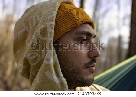Close up photo of young man with hat at outside. Forest background. Sportswear. He looks sad.