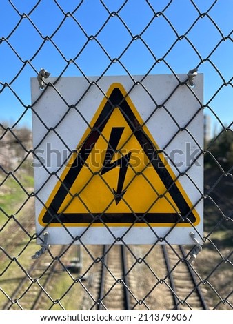 High voltage warning sign mounted on steel wire mesh fence. Special symbol that warns people about voltage and provides security. Warning sign installed on chain-link fence