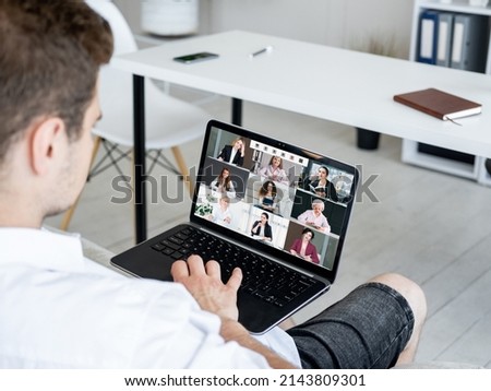 Group video call. Remote meeting. Wfh telecommuting. Relaxed man using laptop working from home online with female business team on screen.