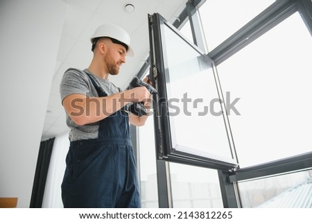 Workman in overalls installing or adjusting plastic windows in the living room at home Royalty-Free Stock Photo #2143812265