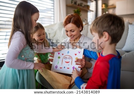 Mother of little children in costumes getting present from them at home.