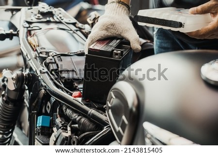  mechanic replaces motorcycle battery and holding Acid pack or sealed battery electrolyte pack to prepare for fill up battery, motorcycle maintenance and service and repair concept . selective focus Royalty-Free Stock Photo #2143815405