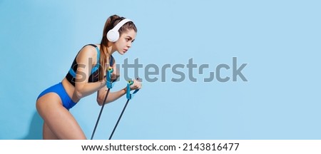 Music and sport. One young beautiful sportive girl in sports uniform training with sports equipment isolated on blue background. Motion, action, motion, beauty concept. Fitness, healthy lifestyle