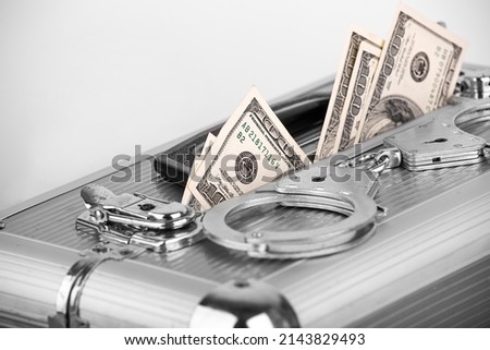 Handcuffs lying on a briefcase with dollars sticking out of it