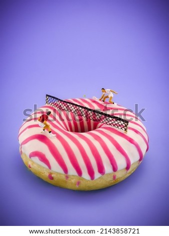 Donut in pastel pink color, on a blue purple background. Tennis players playing game on a sweet doughnut, conceptual photography with miniature figurines. Pastel bright image, color of the year.