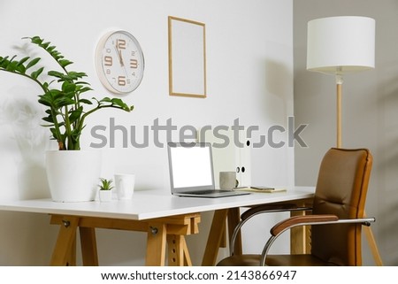 Workplace with modern laptop, cup and houseplant near light wall in office interior