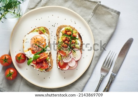 Vegetarian egg sandwiches on white background. Healthy vegetarian sandwiches with egg tomatoes avocado cream and cheese garnished with chia seeds and aromatic herbs. Vegetarian sandwich. Royalty-Free Stock Photo #2143869709