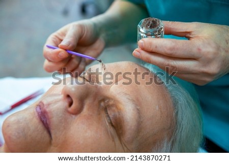 Senior woman getting her eyebrows colored by a beautician in a beauty salon. Elderly female Dye grey eyebrows for younger look. Close up