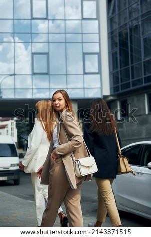 Positive women in formal wear is outdoors in the city together.
