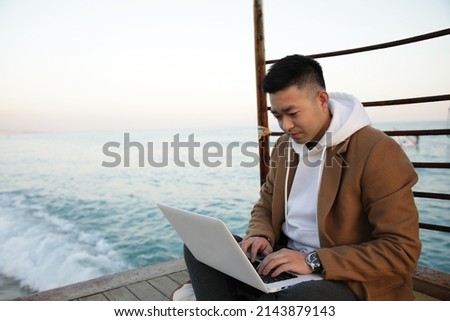 Relaxed young Asian man using laptop on the beach.