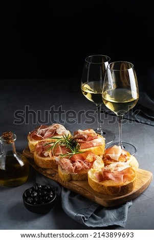 Italian appetiser - bruschetta with prosciutto, white wine, rosemary branch, olive oil and black olives Royalty-Free Stock Photo #2143899693
