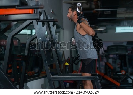 Picture in mirror of a strong muscular fit man training back muscles with weights on the machine in the gym