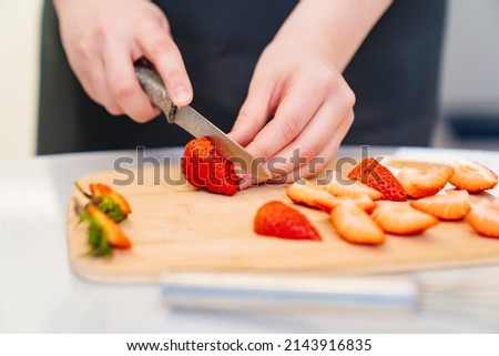 strawberries are cut into pieces on a wooden cutting board to decorate desserts. natural fresh fruits and berries for decorating cakes and cupcakes. recipes for cooking at home. chopped strawberries Royalty-Free Stock Photo #2143916835