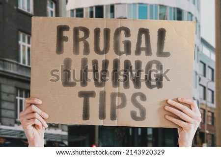 The phrase " Frugal living tips " on a banner in men's hands with blurred background. Bankrupt. Sad. Unhappy. Cheap. Negative. Painful. Hurt. Skills. Strength. Success. Expense. Value. Rate. Bad