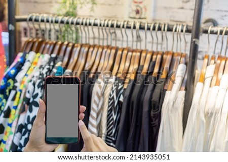 Woman's hand holding a phone in clothing store, blurred clothing store background, shopping online concept.