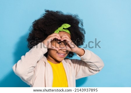 Portrait of attractive funny cheerful girl schoolkid showing heart shape look see spy isolated over bright blue color background