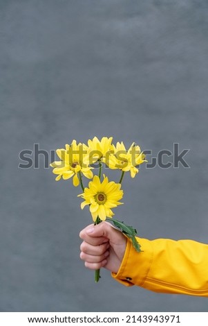 Front view of woman wearing a yellow raincoat holding a flower bouquet. Vertical detail of daisy flowers bouquet isolated on grey wall. Flowers isolated in background concept.