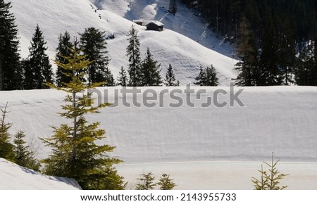 a dam of a frozen lake in the snowy mountains with trees under a blue sunny sky in winter in austria