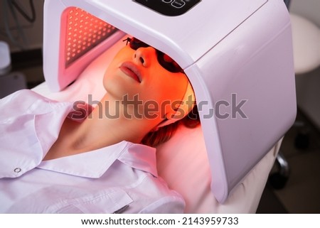 Express facial treatment with led therapy. Beautiful girl on a light therapy procedure. LED lamp with red light. Safe skin care. Royalty-Free Stock Photo #2143959733