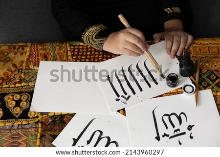 close up muslim girl hands writing Arabic text with bamboo pens and black ink on paper, Arabic letters mean the name of Muslim god "Allah"