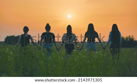 Girls stand holding hands at sunset on a summer evening.