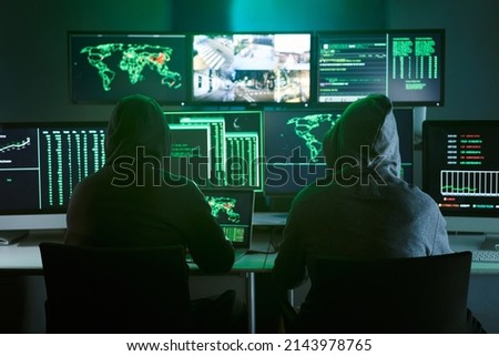 Control room monitoring surveillance video camera control city - Two Hooded hackers in dark room office full device from secret service public safety computer station center. No people indoors. 