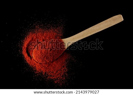 Red paprika, pepper powder in wooden spoon pile isolated on black, top view 