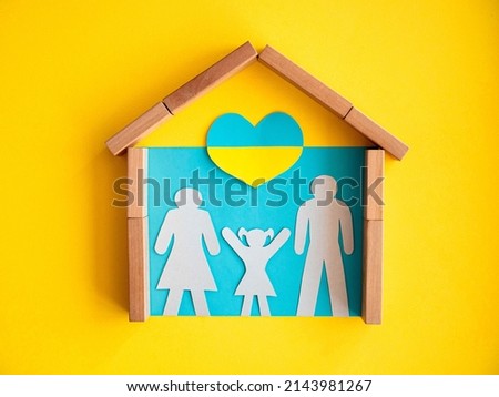 Silhouette of a family in a house on blue in a yellow frame. The girl raised her hands up to a heart in the color of the Ukrainian flag. The concept of housing for the Ukrainian people of refugees.