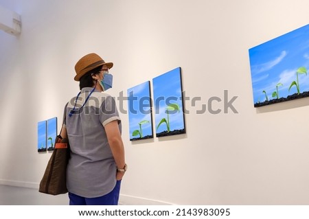 Perspective side view of hipster woman looking at pictures of seedlings growing in germination sequence on white wall in art gallery, world environment day concept, pictures on the wall are my work.