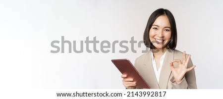 Image of successful asian businesswoman holding digital tablet, showing okay, ok sign, assuring client, standing over white background