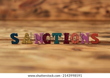 Wooden cubes with the word SANCTION stand on a wooden background between a magnifying glass and a pen. High quality photo