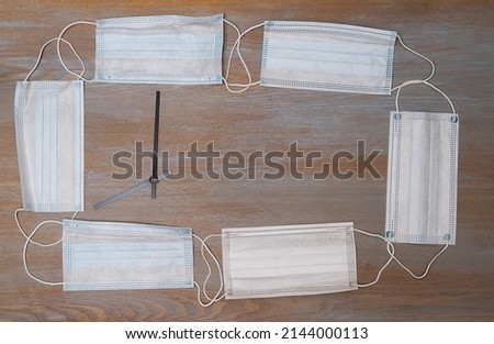 Medical protective masks are laid out along the edge of a wooden table in the form of a frame for text. Studio photography.