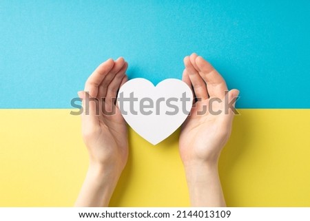 Stop the war in Ukraine concept. Top overhead view photo of girl's hands demonstrating white heart over national flag