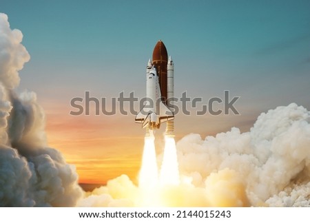Spaceship lift off. Space shuttle with smoke and blast takes off into space on a background of sunset. Successful start of a space mission. Travel to Mars. Elements of this image furnished by NASA. Royalty-Free Stock Photo #2144015243