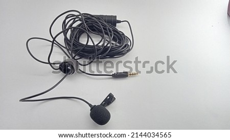 long cable clip-on mic isolated on white background. Small lavalier microphone with clip. Professional sound recording equipment. Lapel mic.