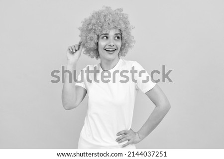 cheerful funny girl with fancy look wearing orange hair wig on yellow background, cool
