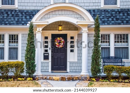 Bluish Grey cedar shake shingled home with drama added by gently curved gable porch roof in early spring with pansies in flower beds and no soliciting sign on hanging mail box