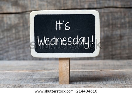 Small wooden framed blackboard on wooden background with text It's Wednesday