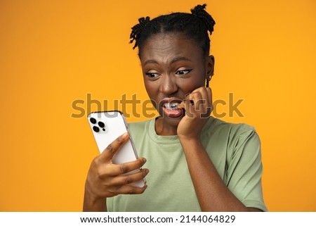 Scared african american woman holding mobile phone seeing bad news against yellow background Royalty-Free Stock Photo #2144064829