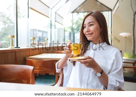 Portrait image of a beautiful young asian woman holding and drinking coffee in cafe