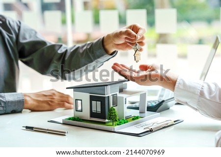 The real estate agent gives the buyer the house keys on a table with modern miniature house model. Royalty-Free Stock Photo #2144070969