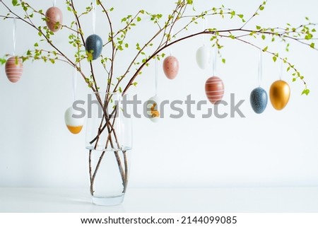 vase with spring branches of blossoming trees, colorful Easter eggs on a white table against a light wall