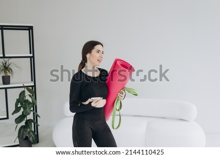 Pretty young sportswoman holding fitness mat while standing at home