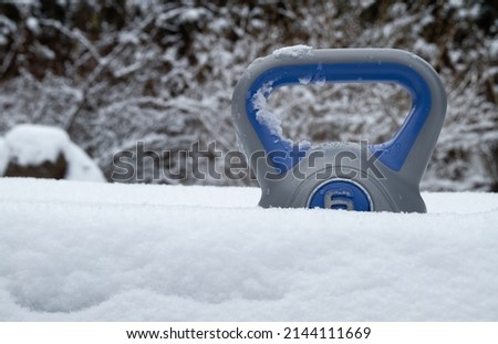 Kettlebell weight in a deep snow. Heavy equipment for home gym workout. Strength training fitness kettlebells, exercise kettle bell with grip handle. Healthy lifestyle seasonal winter scenery.