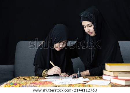 muslim mother with her daughter writing Arabic text with bamboo pens and black ink on paper, Arabic letters mean the name of Muslim god "Allah"