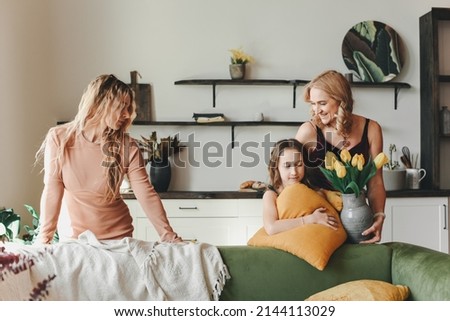 Three beautiful girls in dresses are posing in the studio with flowers. Young beautiful mother with her daughters. Birthday, family celebration at home. Vase with yellow tulips.